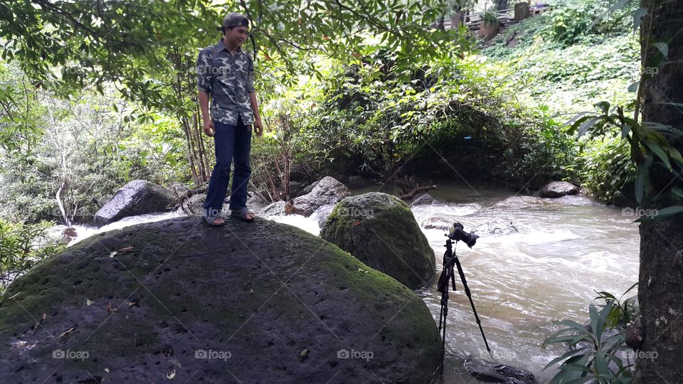 man watching over camera set up on tripod for long exposure photography of a river in the forest