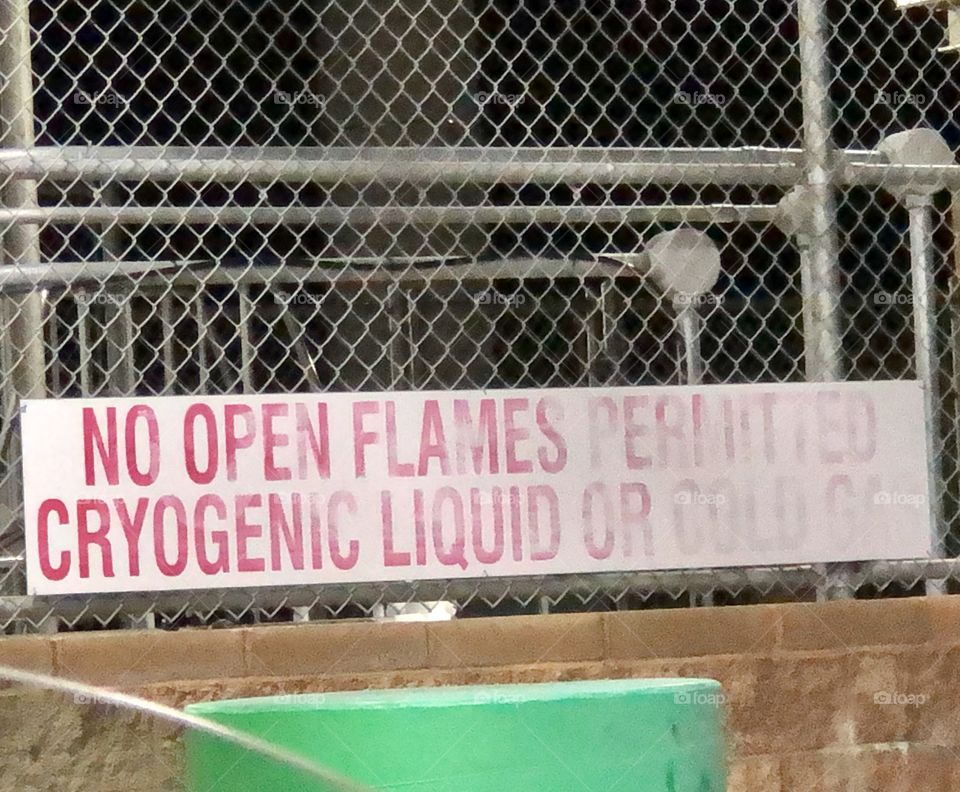 A faded sign at a natural gas gas station surrounded by chain link and oil drums
