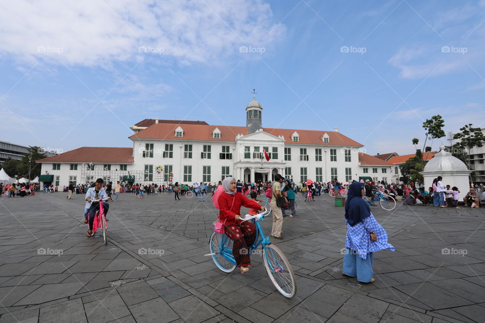 Locals cycle and walk through Fatahillah Square, with Jakarta History Museum in the background, in the Old Town of Jakarta, Indonesia