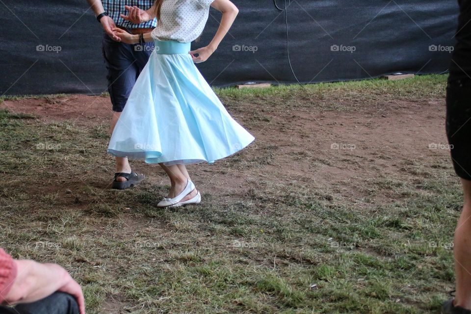 A woman in a light blue swinging petticoat dances with a man on a meadow