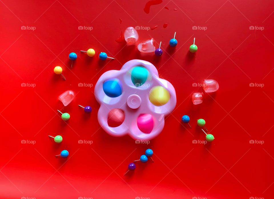 Multicolor Fidget Spinner Time In Motion Long Exposure Seems To create Cold Ice Cubes On A Red Background.