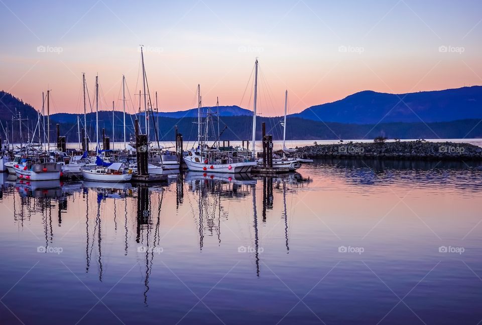 Sailboats docked at small marina after sun has set behind the hills