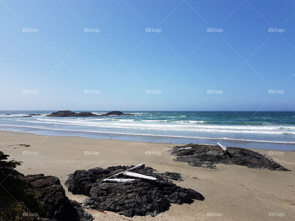 bright sunny clear sky summer day outside, calm sand beach with rocks and white cap waves of the blue ocean