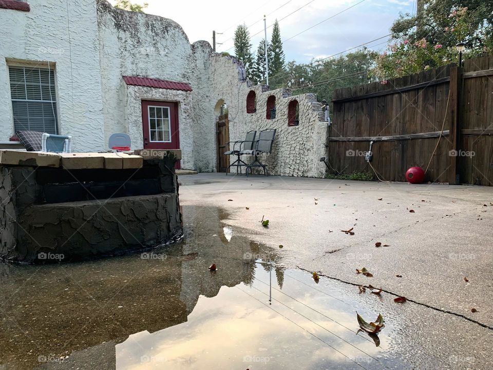 White and red spanish old style architecture residential large house built in the early 1900s. Dark red door with window on the side with aging signs with stairs style wall before sunset with sunlight on top of old well with sky reflection in puddle.