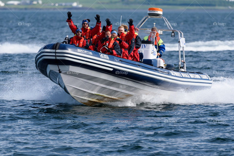 REYKJAVIK, ICELAND - JUNE 3, 2017: Whale and puffin tour boat approaching in full speed in the Atlantic ocean with group of male tourists and guide dressed up in warm overalls and life jackets offshore just outside Reykjavik, Iceland on 3 June 2017.