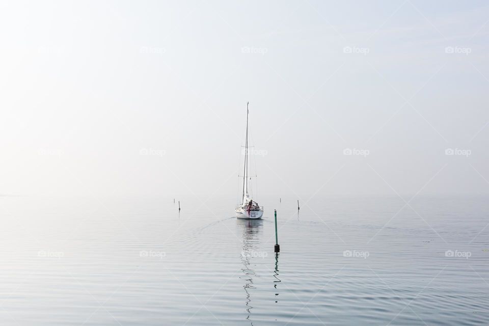 White sailboat on the sea on an early foggy peaceful morning 