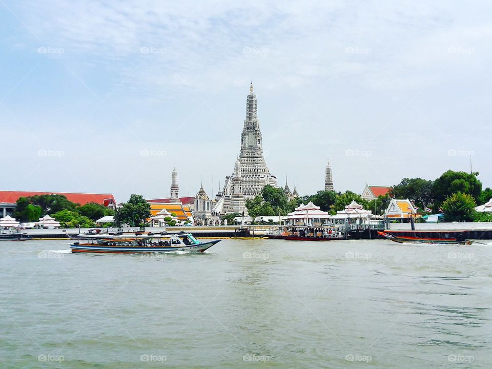 Wat Arun in Bangkok Temple of Dawn

Wat Arun, locally known as Wat Chaeng, is situated on the west (Thonburi) bank of the Chao Phraya River. It is easily one of the most stunning temples in Bangkok, not only because of its riverside location, but also because the design is very different to the other temples you can visit in Bangkok. Wat Arun (or temple of the dawn) is partly made up of colourfully decorated spires and stands majestically over the water. Wat Arun is almost directly opposite Wat Pho, so it is very easy to get to. From Sapphan Taksin boat pier you can take a river boat that stops at pier 8. From here a small shuttle boat takes you from one side of the river to the other for only 3 baht. Entry to the temple is 100 baht. The temple is open daily from 08:30 to 17:30

Although it is known as the Temple of the Dawn, it's absolutely stunning at sunset, particularly when lit up at night. The quietest time to visit, however, is early morning, before the crowds.

Given beauty of the architecture and the fine craftsmanship it is not surprising that Wat Arun is considered by many as one of the most beautiful temples in Thailand. The spire (prang) on the bank of Chao Phraya River is one of Bangkok's world-famous landmarks. It has an imposing spire over 70 metres high, beautifully decorated with tiny pieces of coloured glass and Chinese porcelain placed delicately into intricate patterns.

You can climb the central prang if you wish, the steps are very steep but there is a railing to balance yourself. Getting up is as tricky as getting down! When you reach the highest point you can see the winding Chao Phraya River and the Grand Palace and Wat Pho opposite. Along the base of this central tower there are sculptures of Chinese soldiers and animals.

Head into the ordination hall and you can admire a golden Buddha image and the detailed murals that decorate the walls. Although Wat Arun is a very popular for tourists, it is also an important place of worship