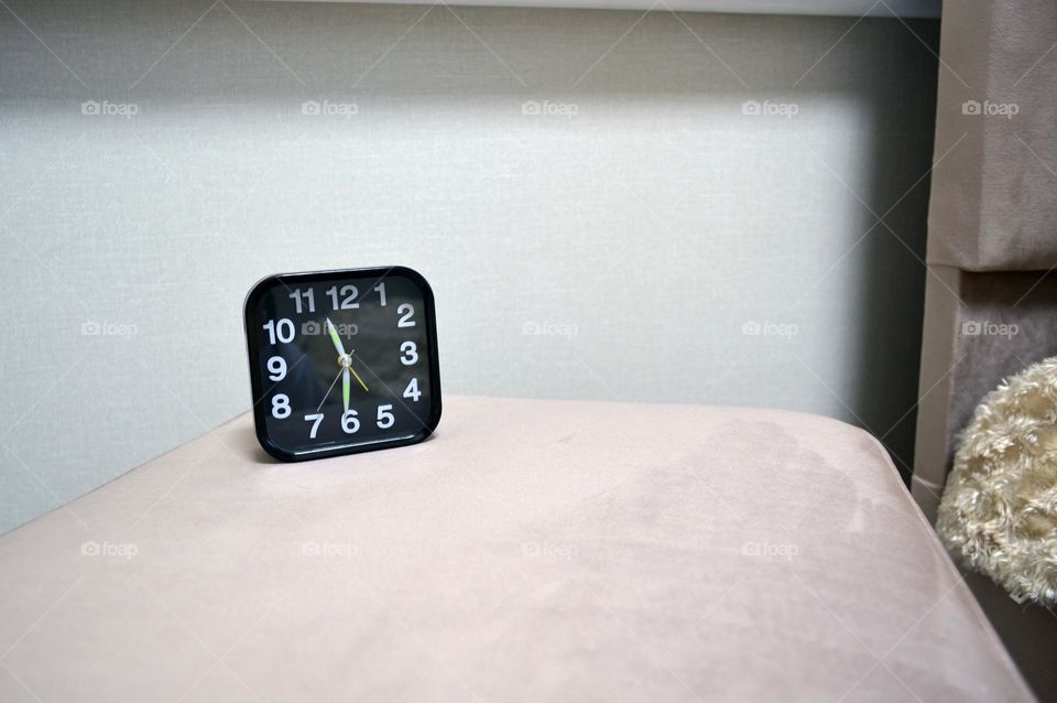 a black clock sits on the ottoman by the bed in the bedroom