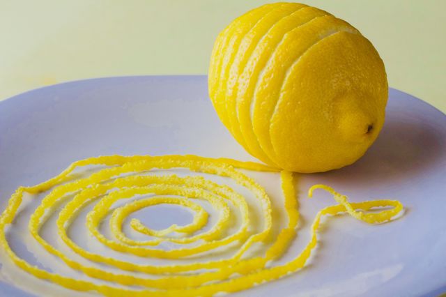 Lemon and spiraled lemon peel on a white plate with yellow background  