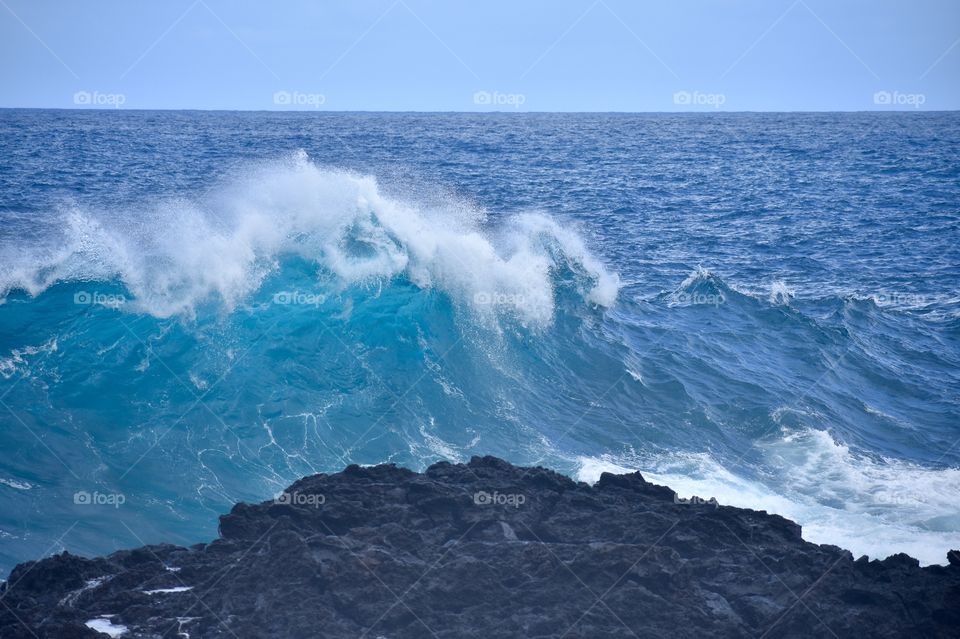 Big wave rising and soon to fall toward the lava rock.