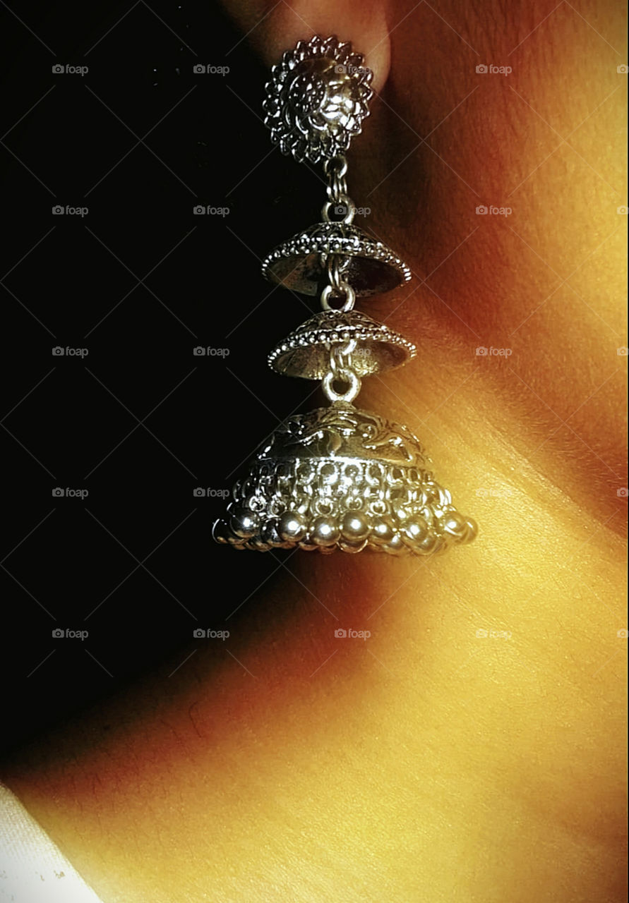 Closeup shot of a beautiful piece of earings worn by a women.Dark background with a contrast of Gold and silver.