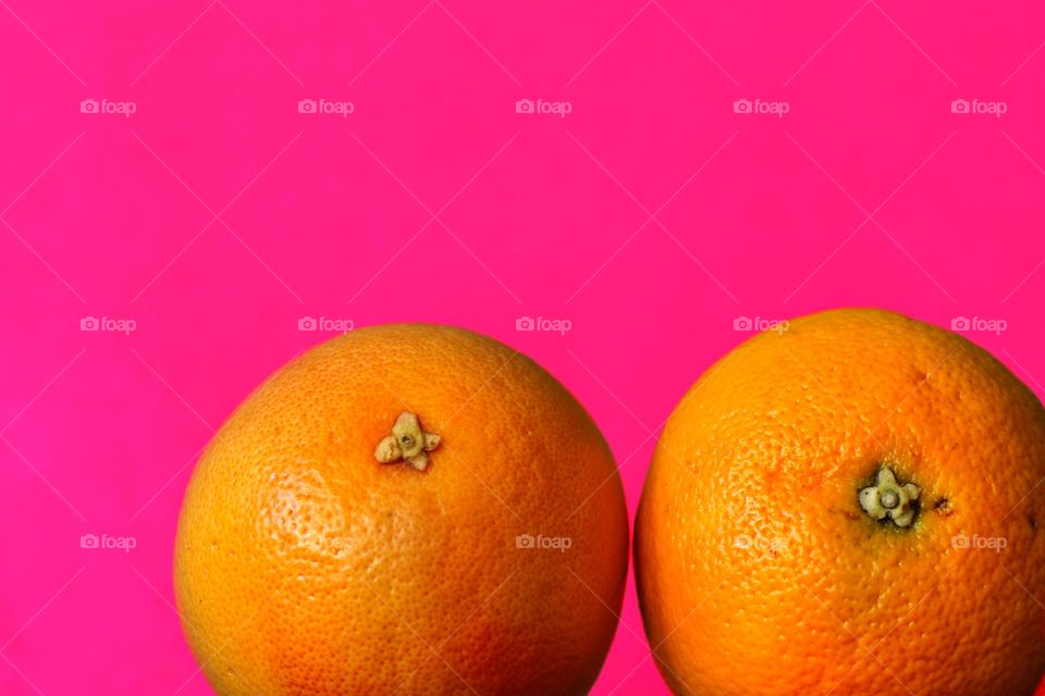 Close up of two orange red grapefruits against pink background