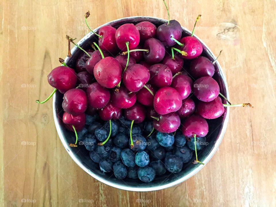 Juicy fresh cherries and blueberries, in a inox bowl on a wooden table