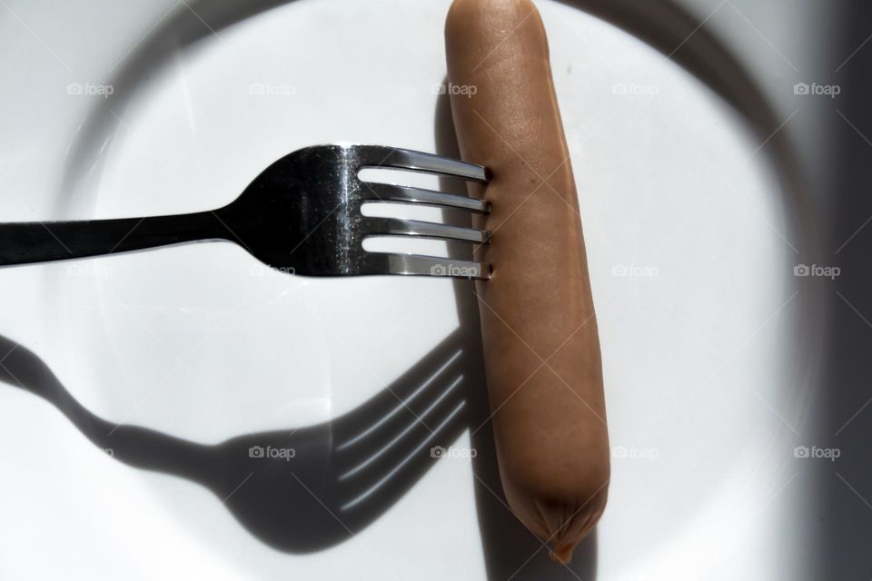 A fork strings a sausage on a white porcelain plate.