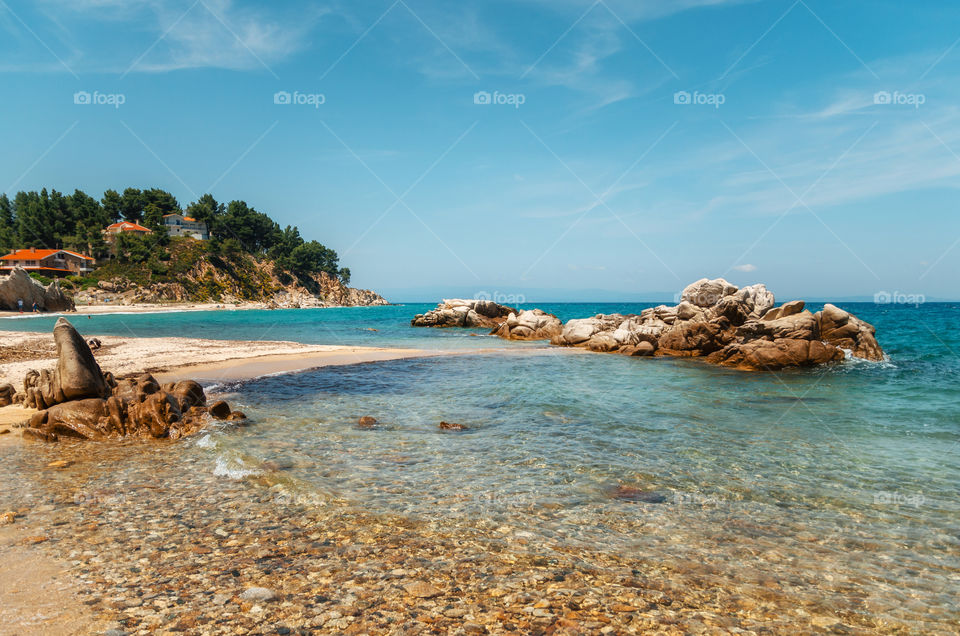 Wild rocky beach with turquoise transparent water and large stones in Vourvourou, Halkidiki, Greece