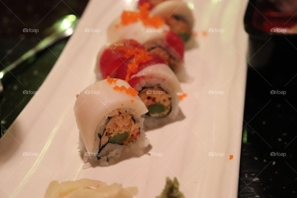 A line or row of different varieties of sushi rolls with raw fish on top with bright contrasts. 