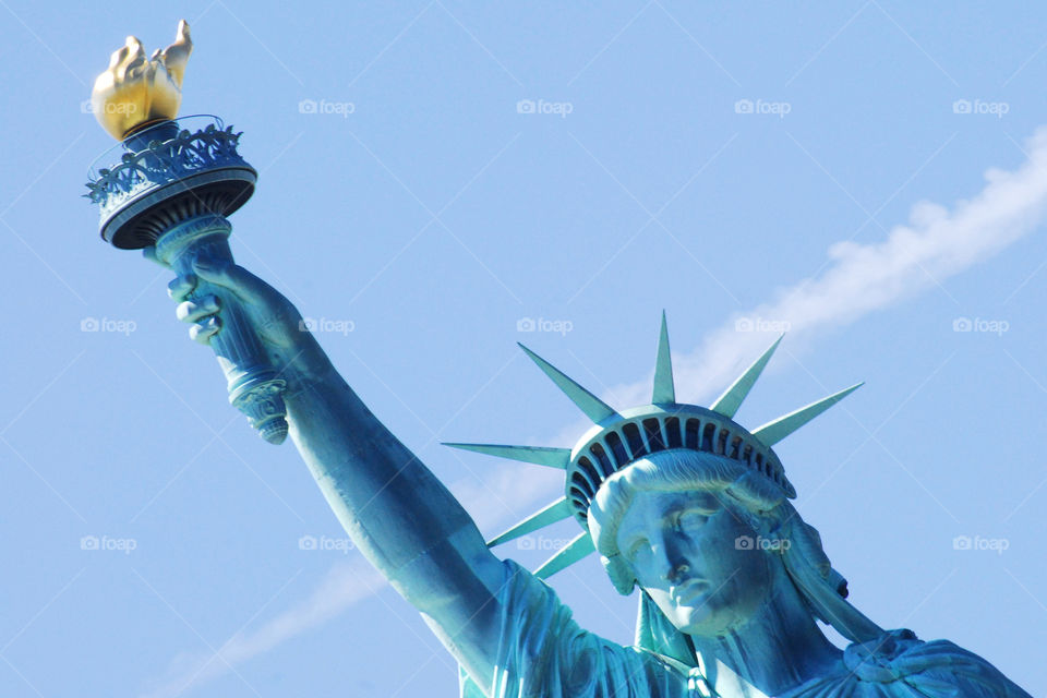 The head and arm of the Statue of Liberty in New York with the blue sky as background