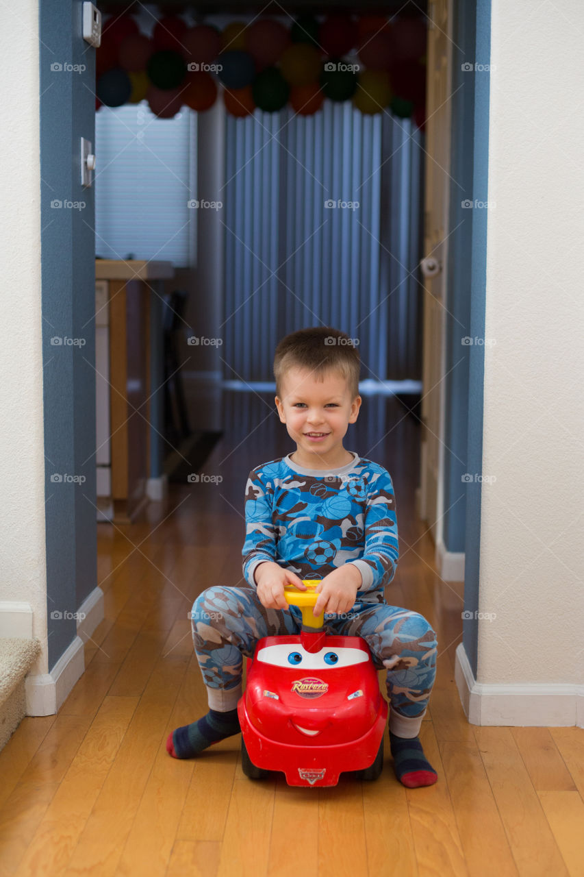 Toddler boy riding toy car inside house 