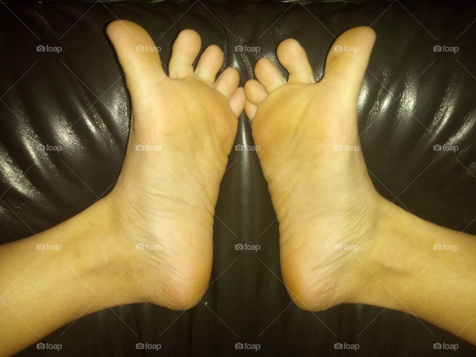 Small feet with soles facing up on leather at night.