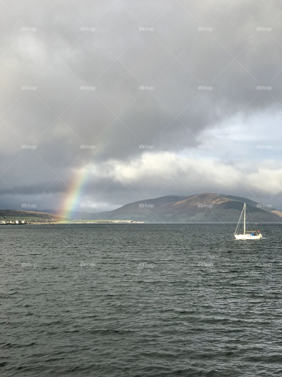 Beautiful rainbow over the bay and a white sailboat at Rothesay, Isle of Bute, Scotland