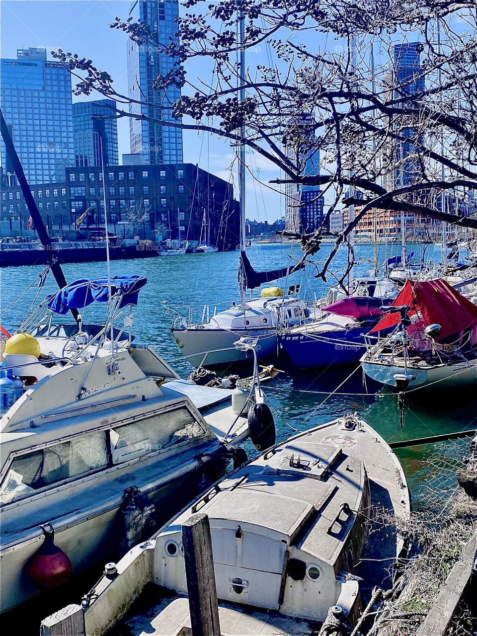 A picturesque view of the boats at “Newtown Creek” in LIC, Queens by the “Pulaski Bridge” up close. The bright turquoise blue of the ocean contrasts against the even brighter fiberglass boats and the sun adds sparkles. 2023. Hypnotic Productions