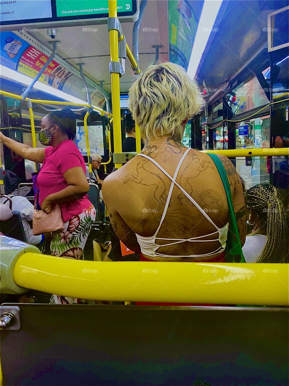 A young lady with bleached hair, a white top and bare back with tattoos is riding the bus home to “Newtown Creek” with me. The combination of neon lights, yellow bars and her striking presence just had to be photographed. 2023. Hypnotic Productions