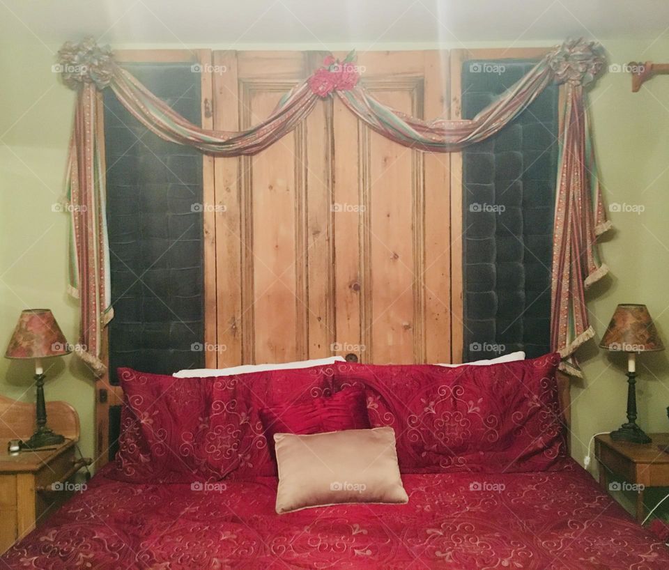 A bedroom in an old bed & breakfast on Prince Edward Island, Canada, exuding old-school charm. The room is filled with warm, nostalgic vibes, featuring an ornate head board and regal red bedding—a cozy and inviting room with a quiet sense of elegance