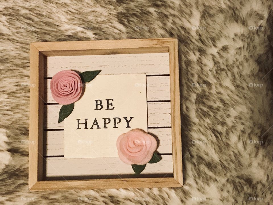 New Years resolutions to be a Happy person !! A wooden sign with beautiful pink roses saying Be Happy written on it displayed on a fuzzy rug. USA, America 