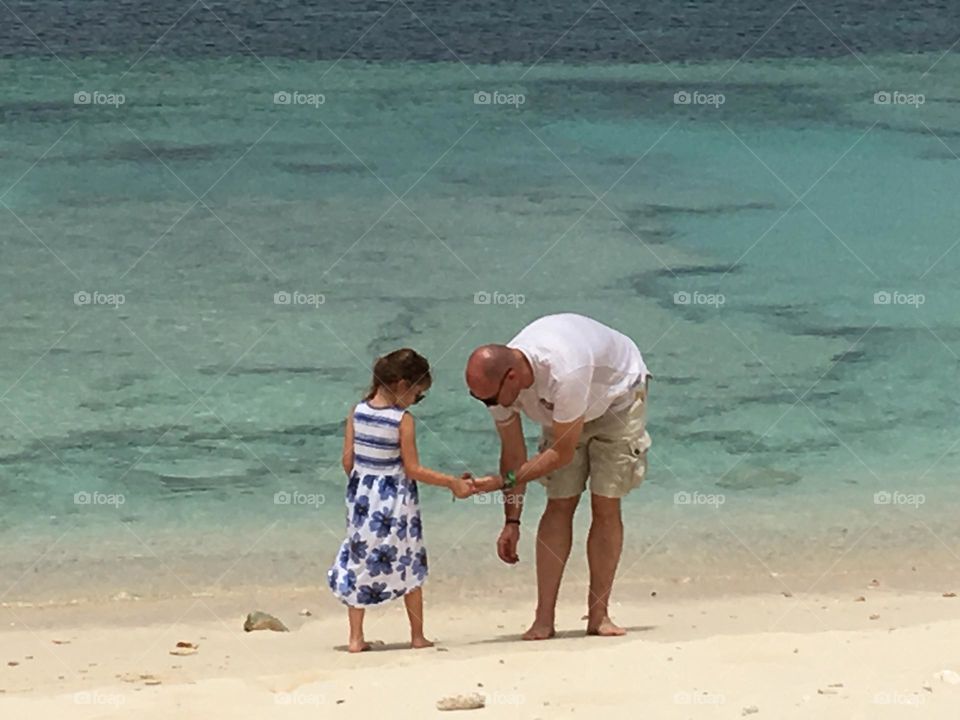 Father and daughter sharing a tender moment with the backdrop of a turquoise sea.