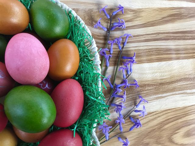 Easter is here, so in this photo you see a bascet full with colorful Easter eggs on the table, with purple hyacint flowers.