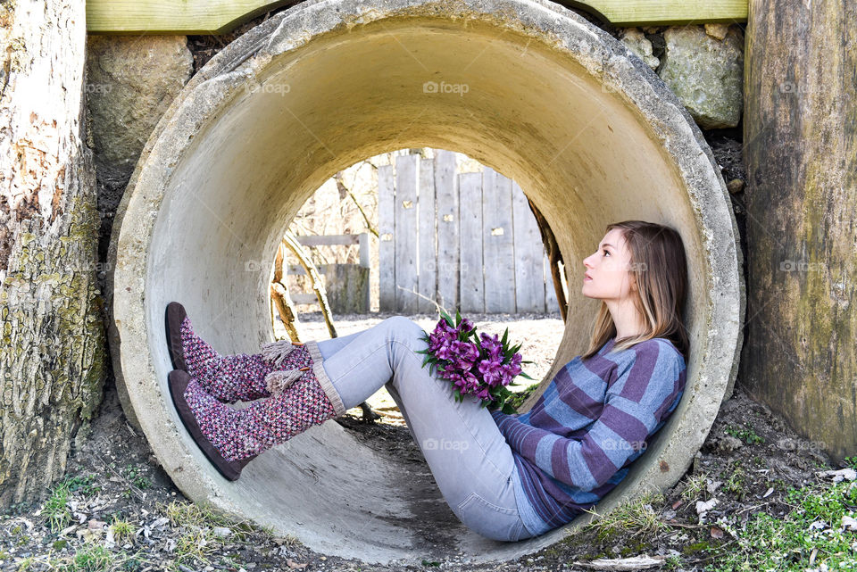 Young woman holding flowers, sitting in a round cement tunnel outdoors