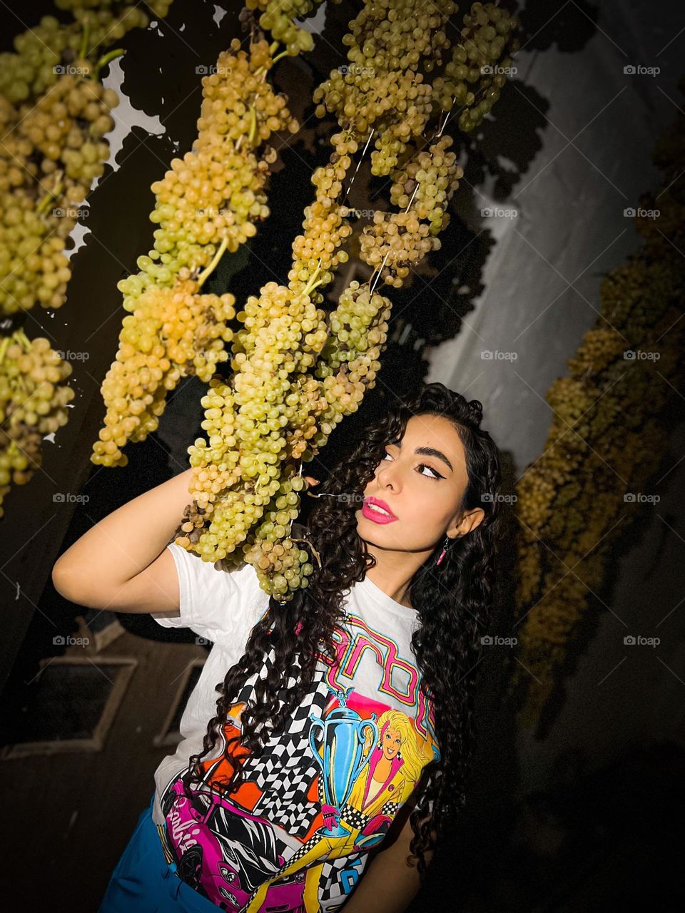 A girl with curly hair next to the bunches of grapes