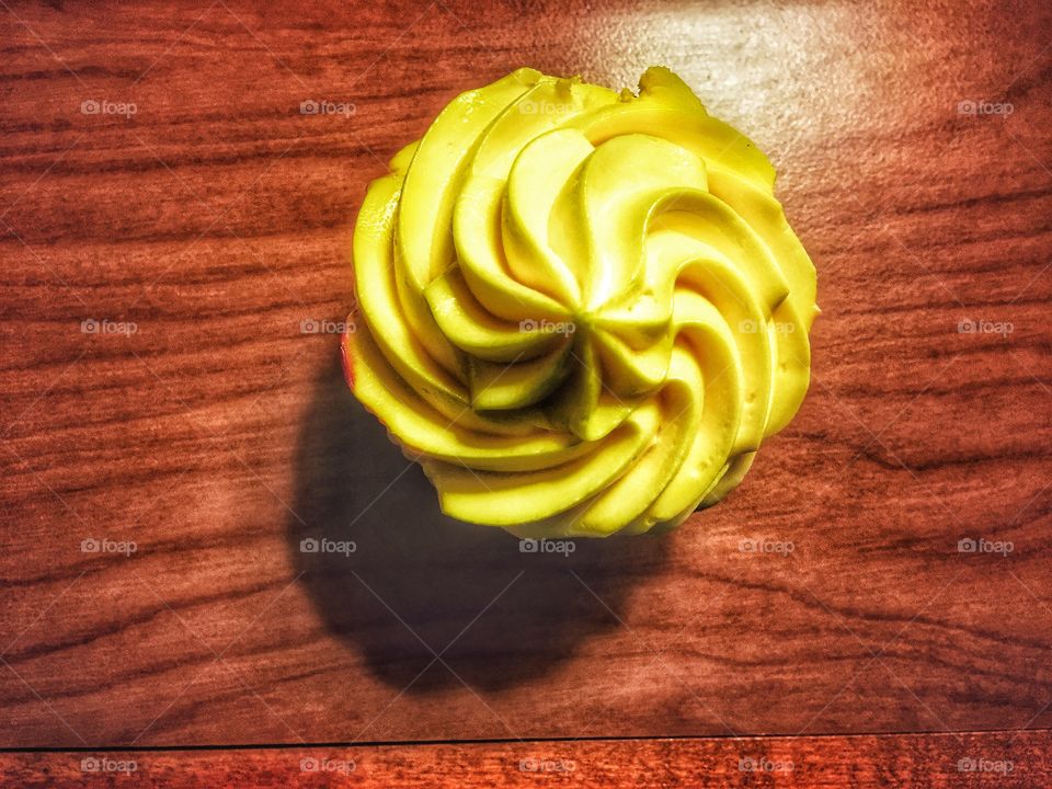 Bright yellow cupcake on a wooden desk 