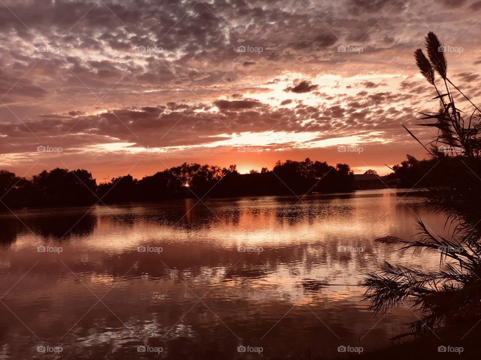 Setting Sun with complex clouds above. The Entire Sky is covered with complex Colours all of which is Total Reflection to lake waters making a Unique silhouetted Beautifully Sunset. Landscape is Totally used in this Pic.
