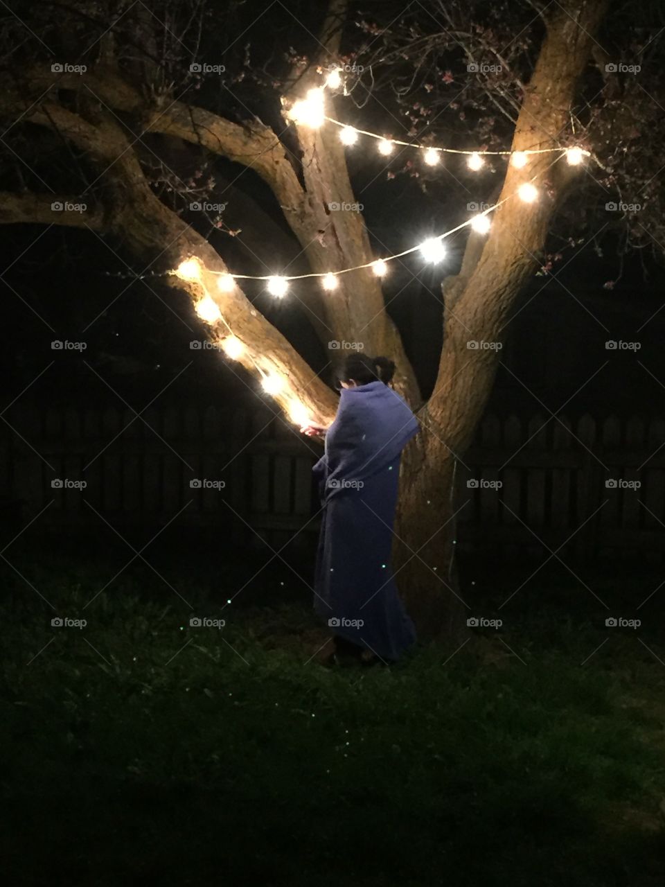 Girl in blanket under tree with lights. 