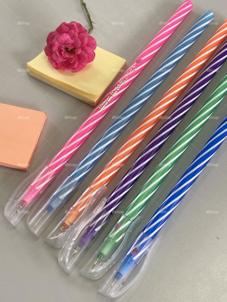 Composição com canetas coloridas, blocos de anotações e para alegrar o cenário uma pequena rosa pink.