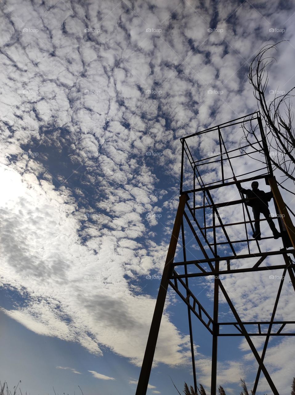 An abandoned old metal construction in Bulgaria up in the blue cloudy skies with a man standing on top of it