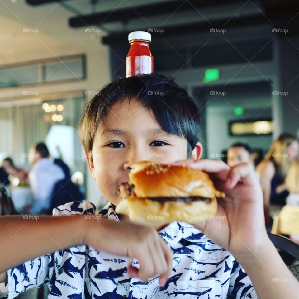 Boy eating dinner with tiny ketchup bottle on his head