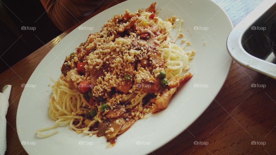 A Chinese pasta dish, which contains munched peanut, chicken, cooked vegetables in say sauce. Served on a white plate.