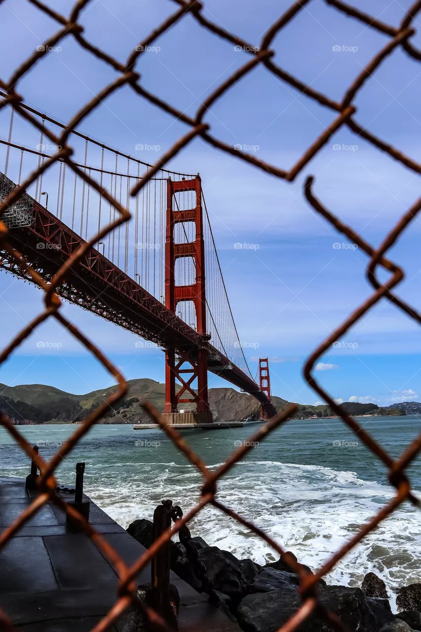 Golden Gate Bridge in San Francisco California seen through a rusty metal wire fence on a clear day still looking majestic at the Fort Point viewing area 