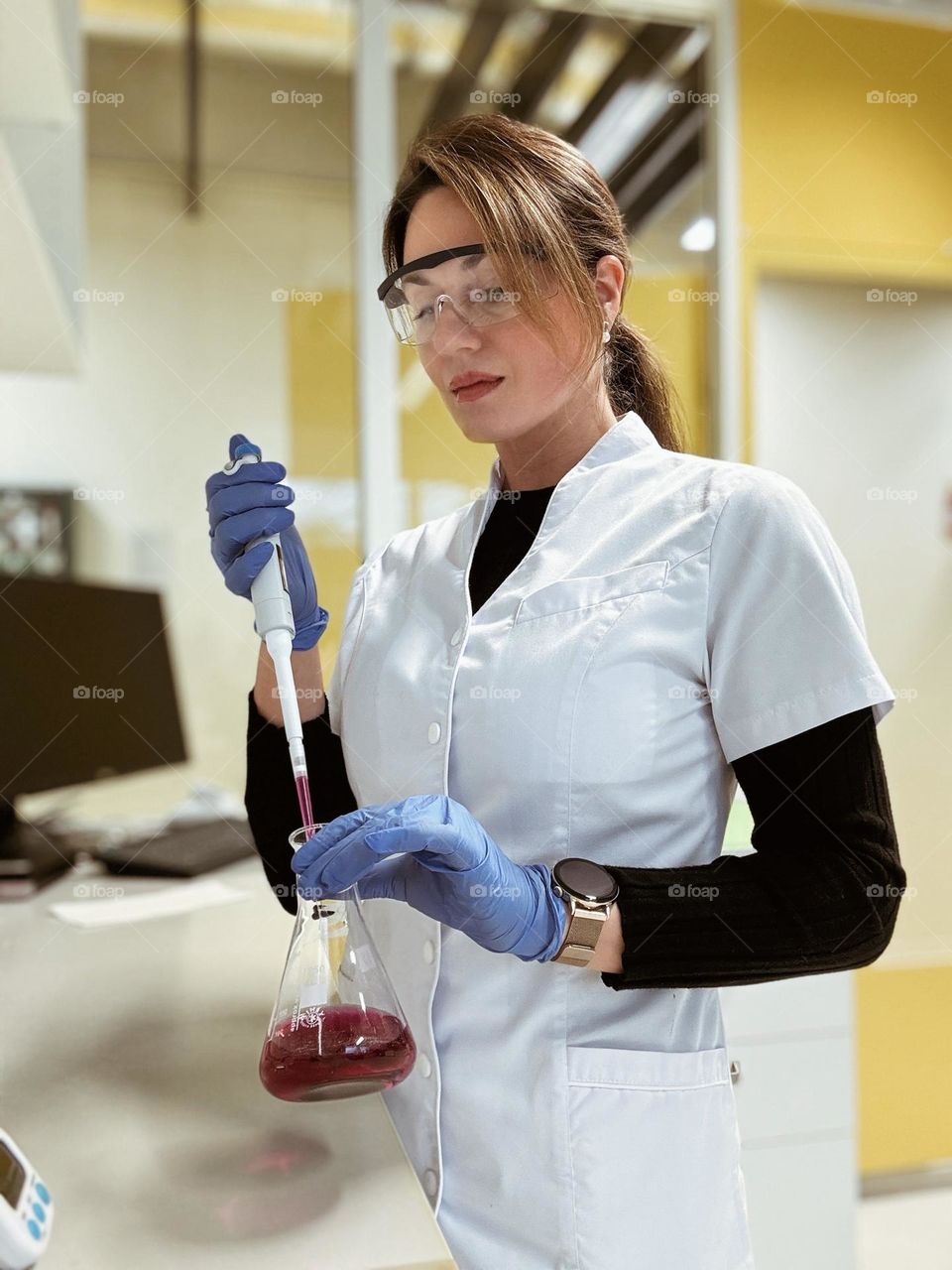 Woman in laboratory pipetting with automatic pipette from conical flask