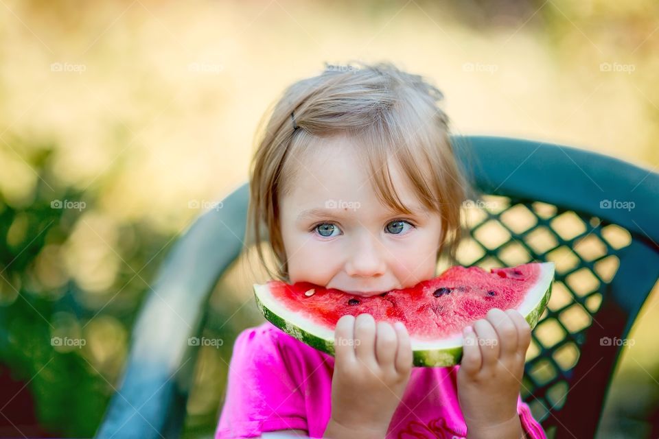 Cute little girl eating watermelon in summer garden 