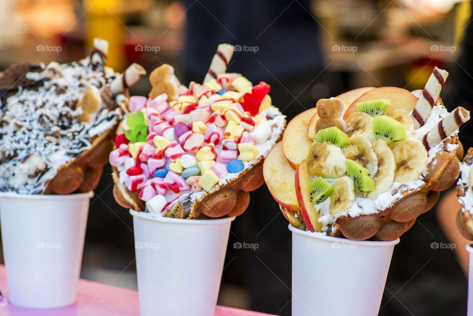 Bubble waffles with raspberries, chocolate and marshmallow in white paper cups are sold on Open kitchen food festival event