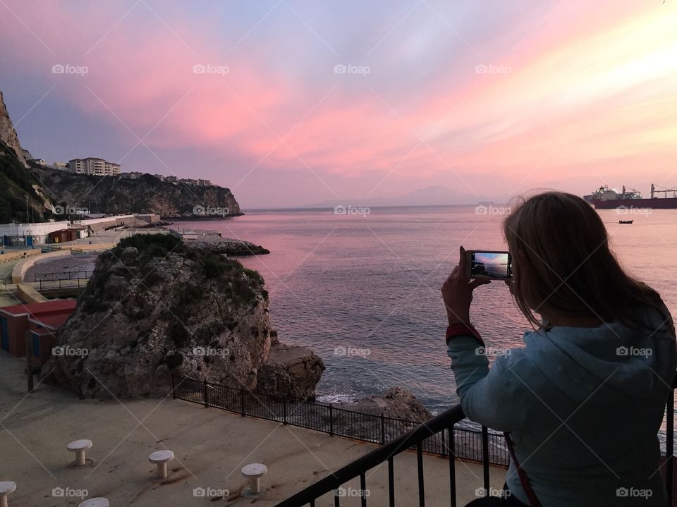 Woman taking photograph of sea during sunset with mobile phone