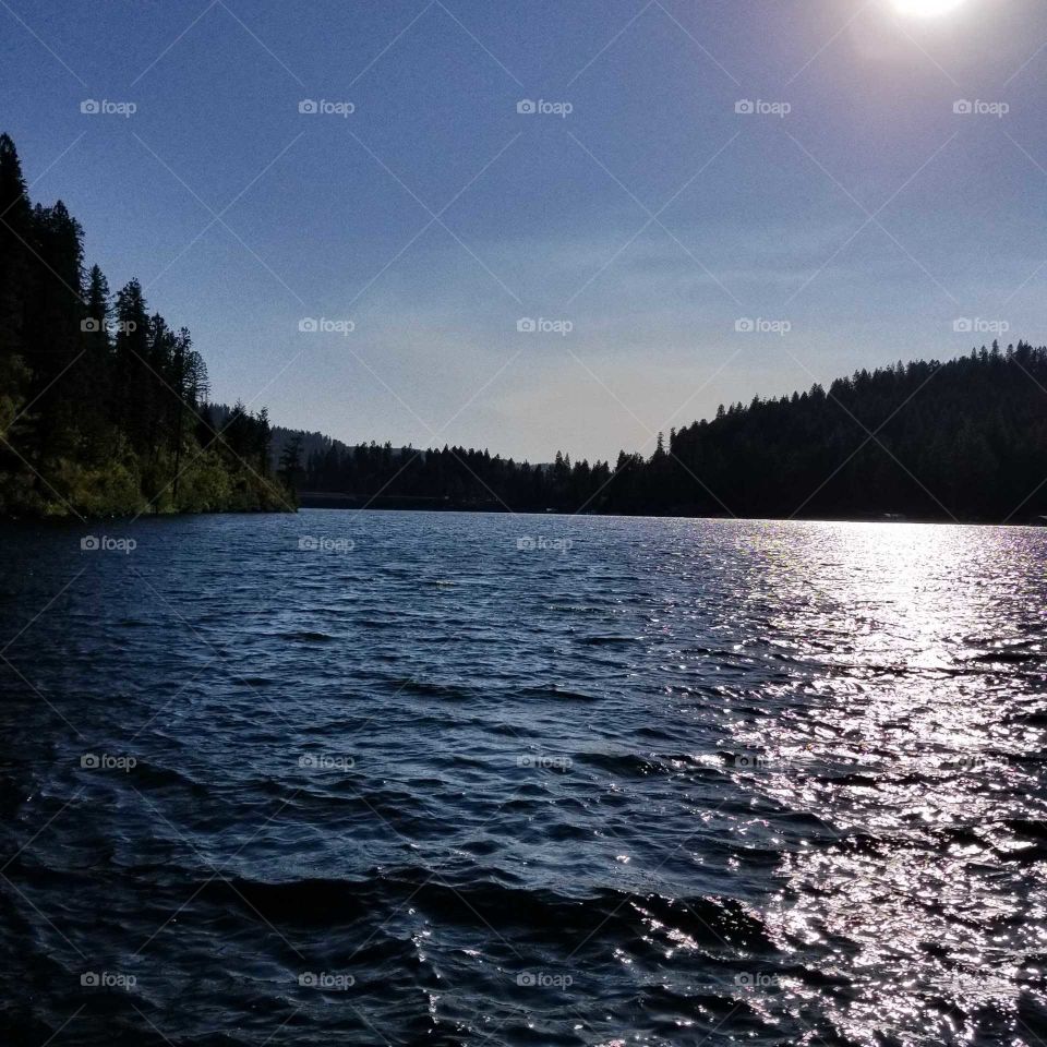 view of sun shimmering on lake water surrounded nmby mountains under a sunny blue sky