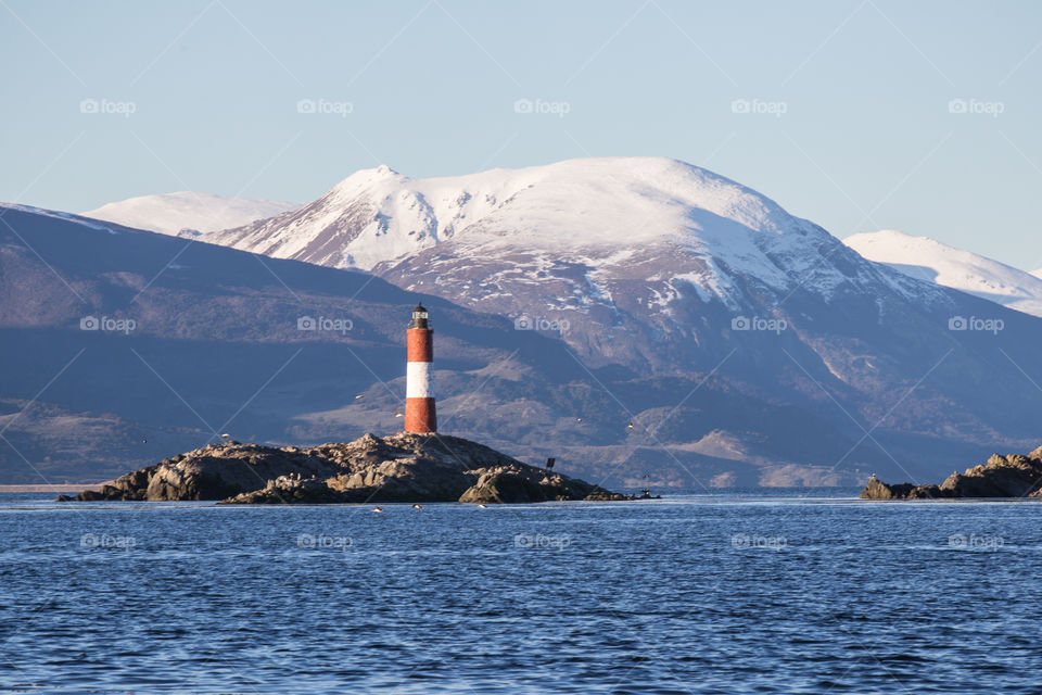 lighthouse on an island with snowy mountain at the back