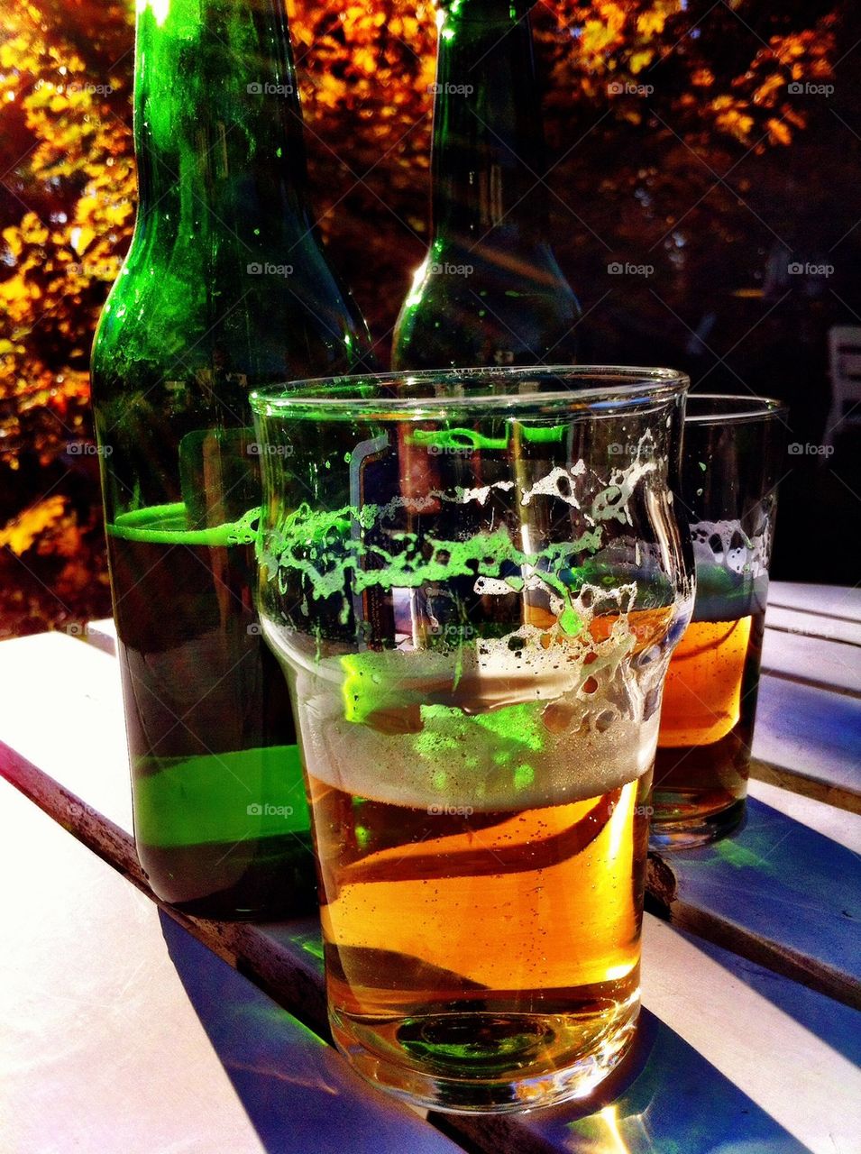 Glasses of beer and bottles outdoors in fall.