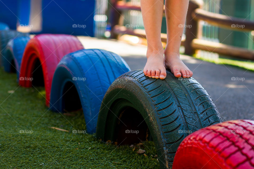 Old car tyres are used in a playground for balance and play. Painted tyres is a great way to recycle. Image of girl standing on recycled wheel tyres.