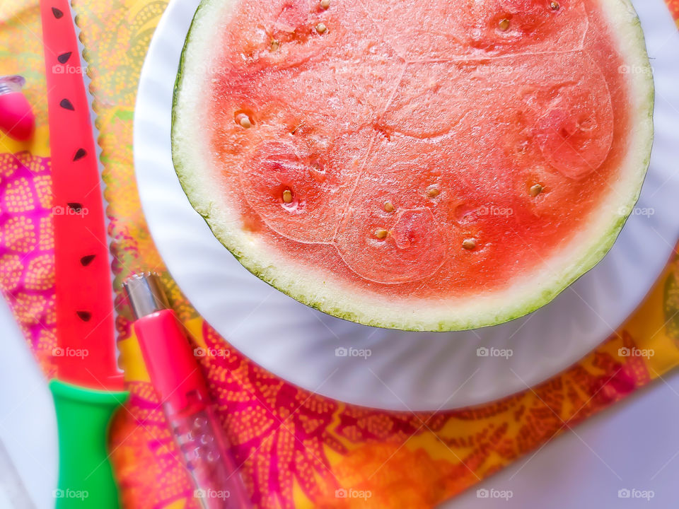 A personal size watermelon half on a white plate on a bright and colorful complementary summer placemat.