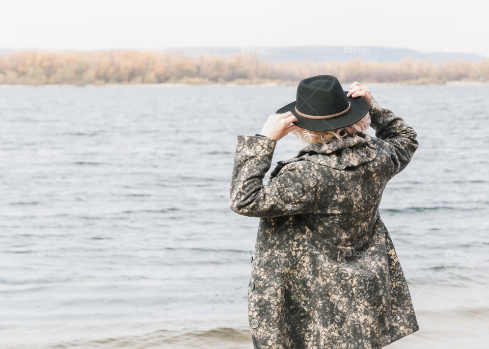 Portrait of stylish adult woman in black hat standing by the river